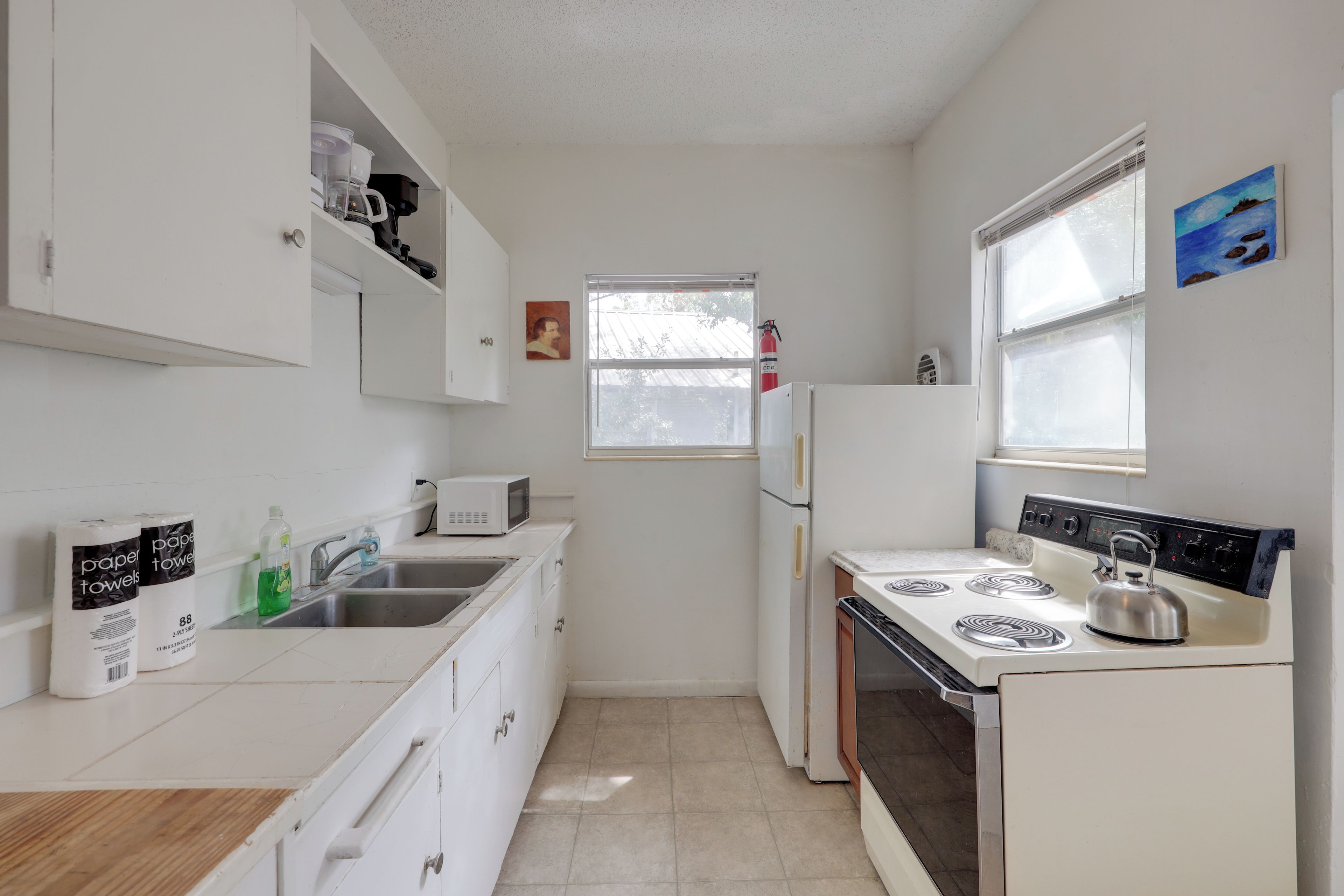 A compact kitchen with white cabinets, a stainless steel sink, a microwave, a stove, and a refrigerator.