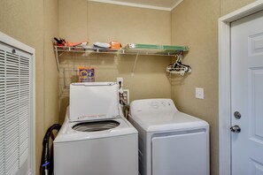 Une buanderie équipée d’un lave-linge et d’un sèche-linge à chargement frontal, d’une étagère contenant des produits de nettoyage et d’une porte située sur le côté droit.