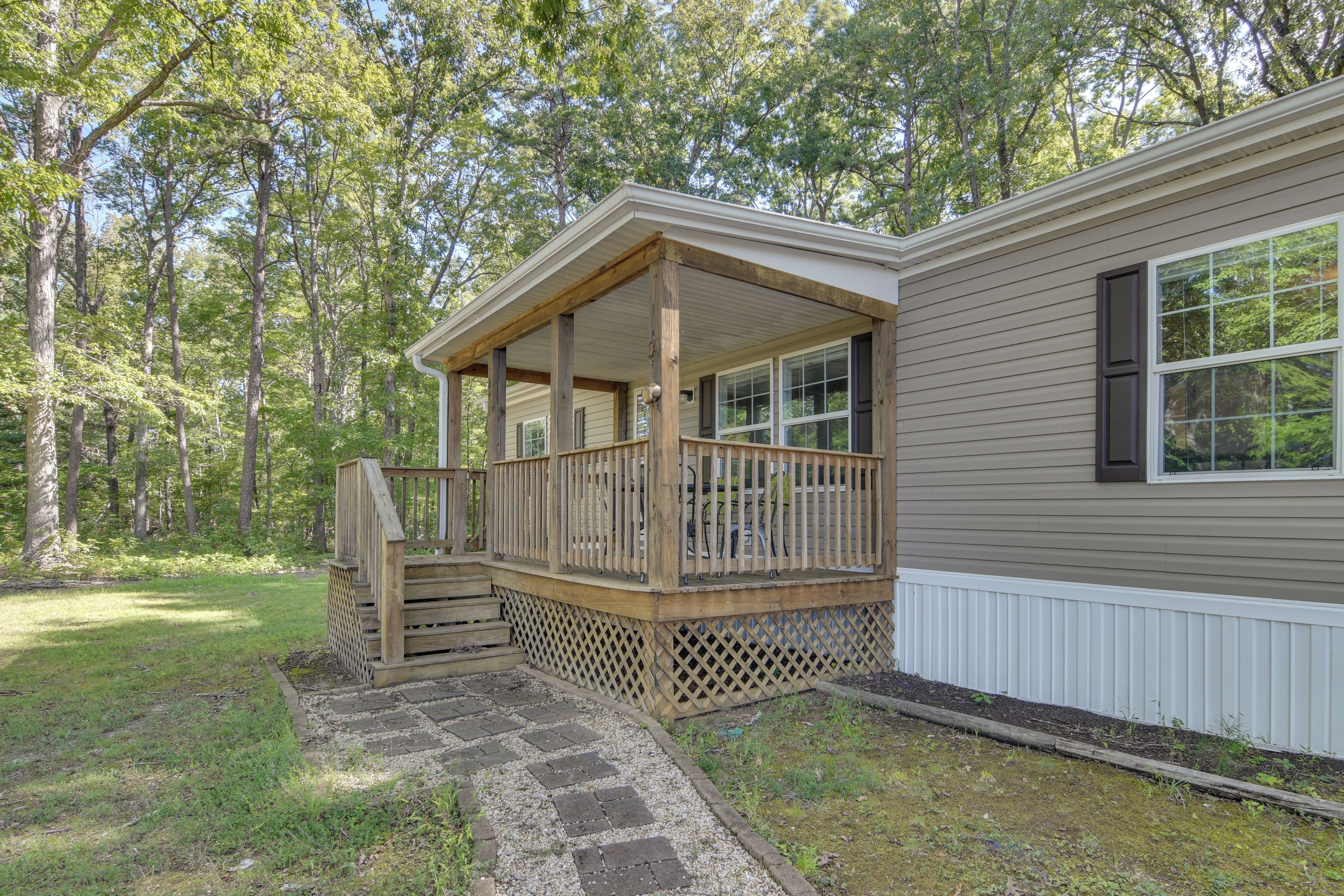 A single-story house with a covered porch, a stone pathway leading to the entrance, and a forested backdrop.