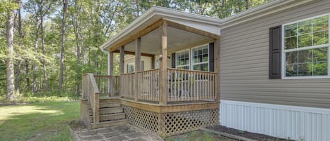 A single-story house with a covered porch, a stone pathway leading to the entrance, and a forested backdrop.
