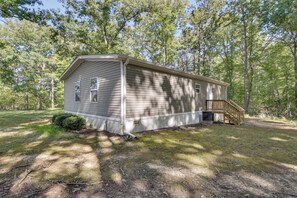 Une cabane de plain-pied avec un porche à l’avant et une petite terrasse, entourée d’une zone boisée.