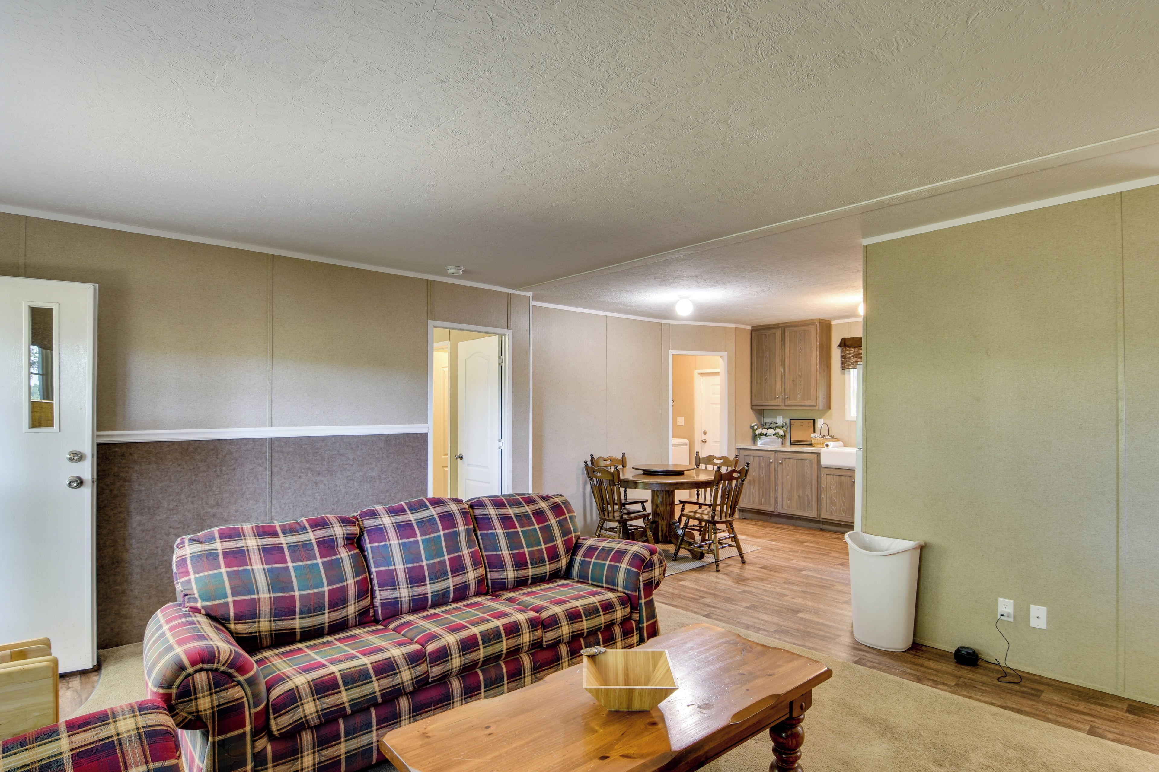 A living room with a plaid sofa, a wooden coffee table, and a dining area with a wooden table and chairs.