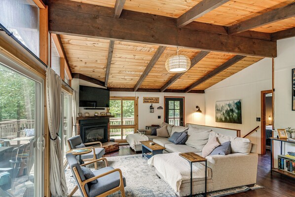 A cozy living room with a fireplace, comfortable seating, and a large window overlooking a deck. - Great for Groups! Wilmington Gem w/ Game Room (Wilmington)