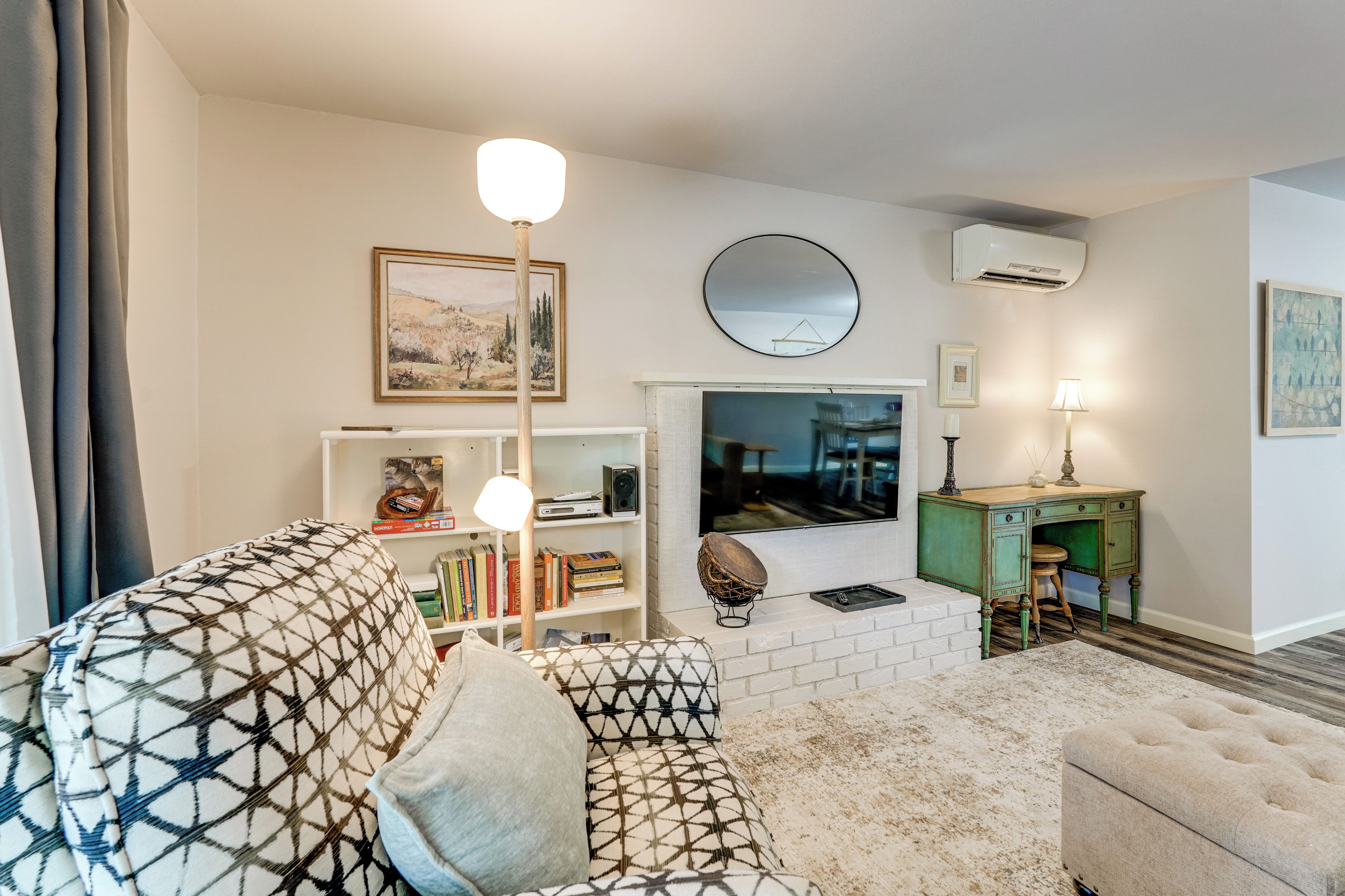Ein Wohnzimmer mit einem gemusterten Sofa, einem weißen Kamin, einem Bücherregal und einem Fernseher.