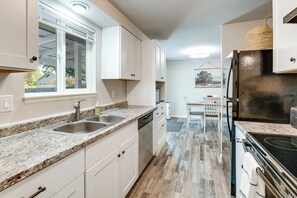 Eine moderne Küche mit weißen Schränken, Granit Arbeitsplatten, einem Edelstahlkühlschrank und einem Essbereich mit Tisch und Stühlen.