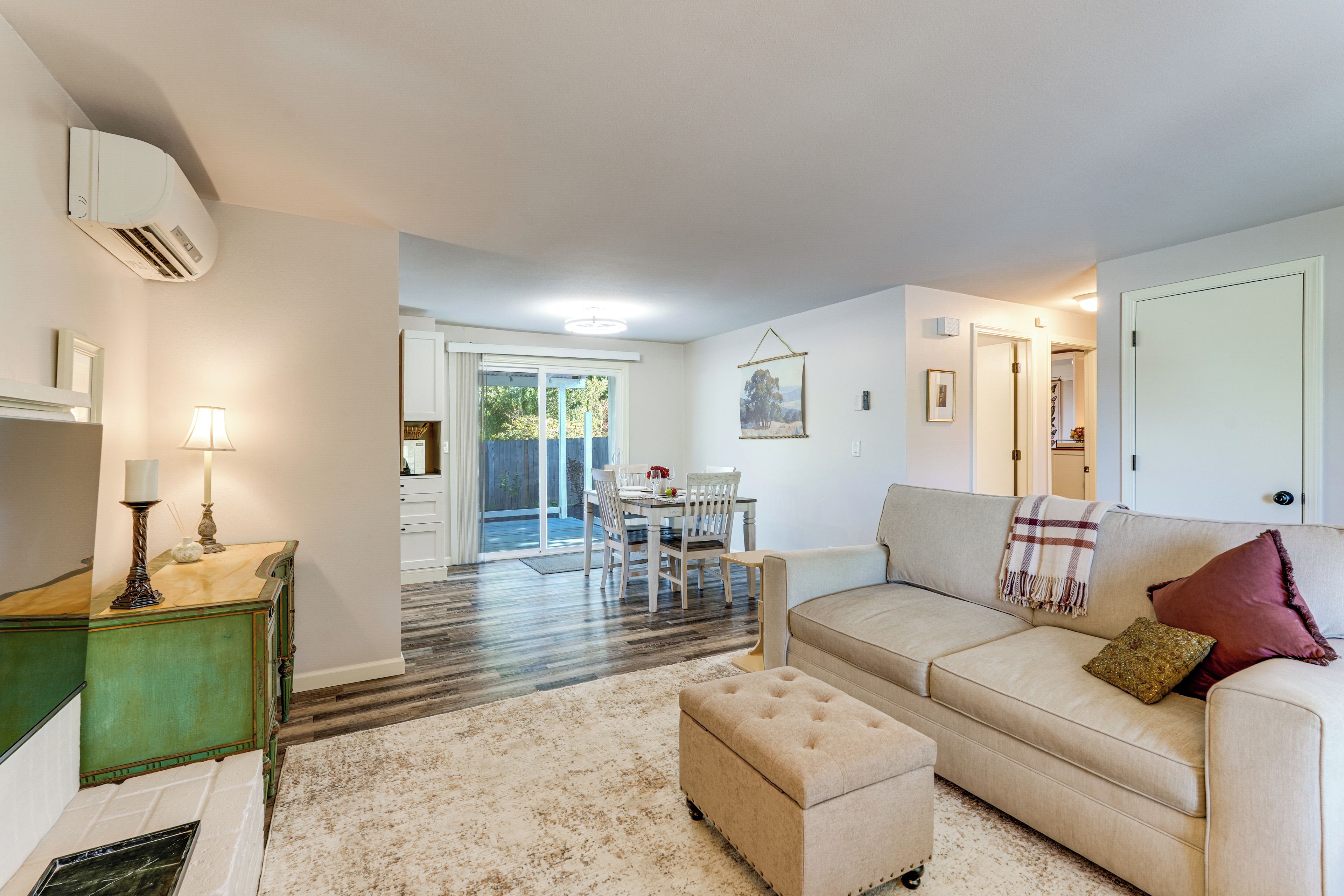 A living room with a beige sofa, a small ottoman, a coffee table, and a dining area with a table and chairs.