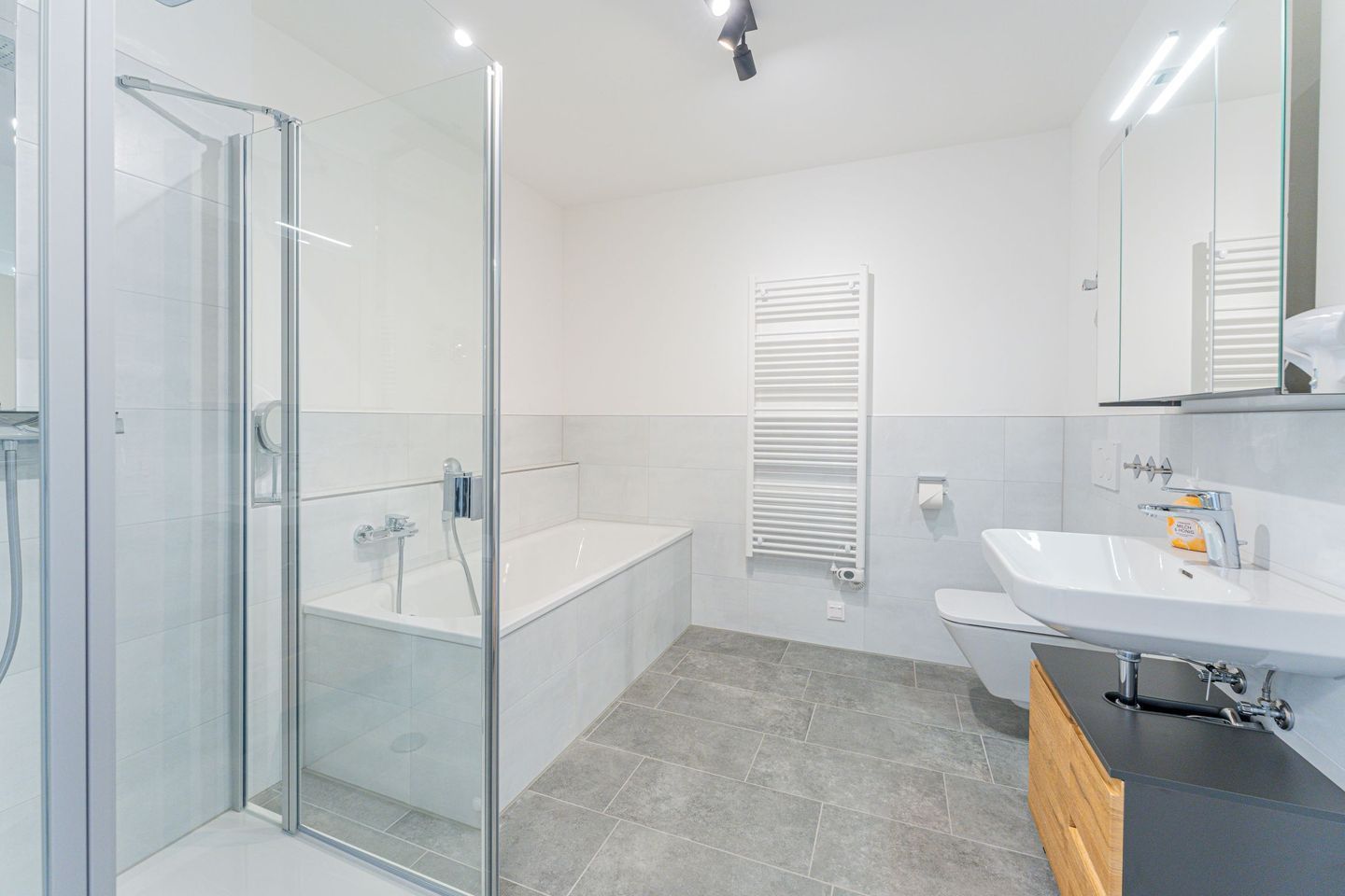 Ein modernes Badezimmer mit Duschkabine aus Glas, einer freistehenden Badewanne, einer Toilette und einem Waschtisch.