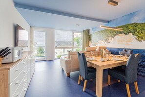Een moderne eethoek met een houten tafel voor vier personen, omringd door stoelen, en een groot raam met uitzicht op de omgeving.