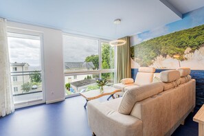 Una sala de estar moderna con un sofá, una mesa y vistas a un paisaje costero a través de grandes ventanales.