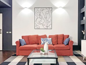 Sala de estar con un sofá rojo, una mesa de centro de vidrio y una obra de arte colgada en la pared.