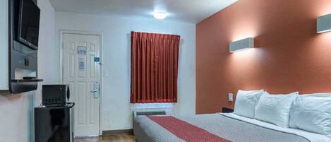 Habitación de hotel con cama, escritorio, televisor y ventana con cortinas.