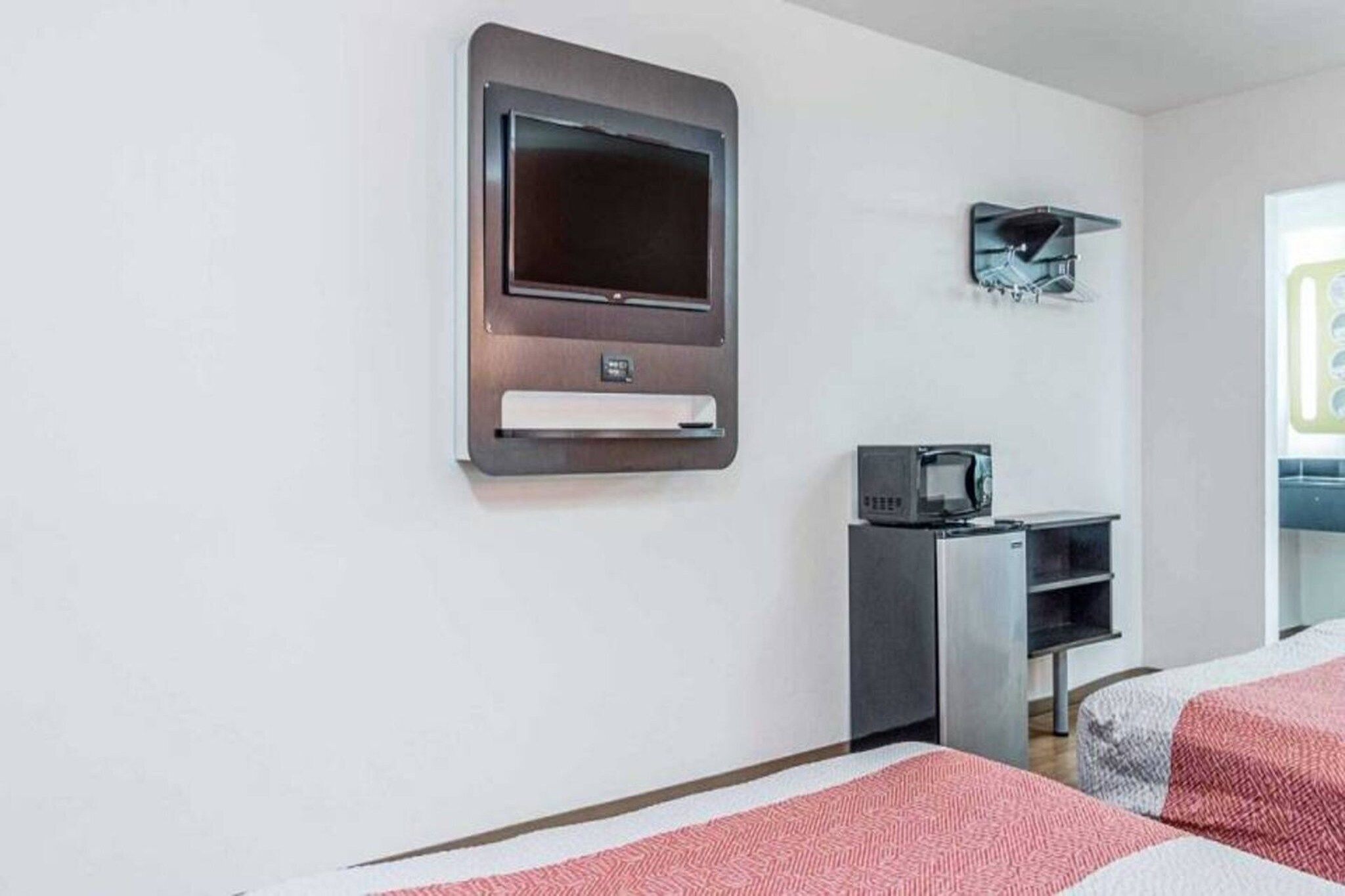 Et hotelværelse med et fladskærms-tv på væggen, en mikrobølgeovn og et køleskab.