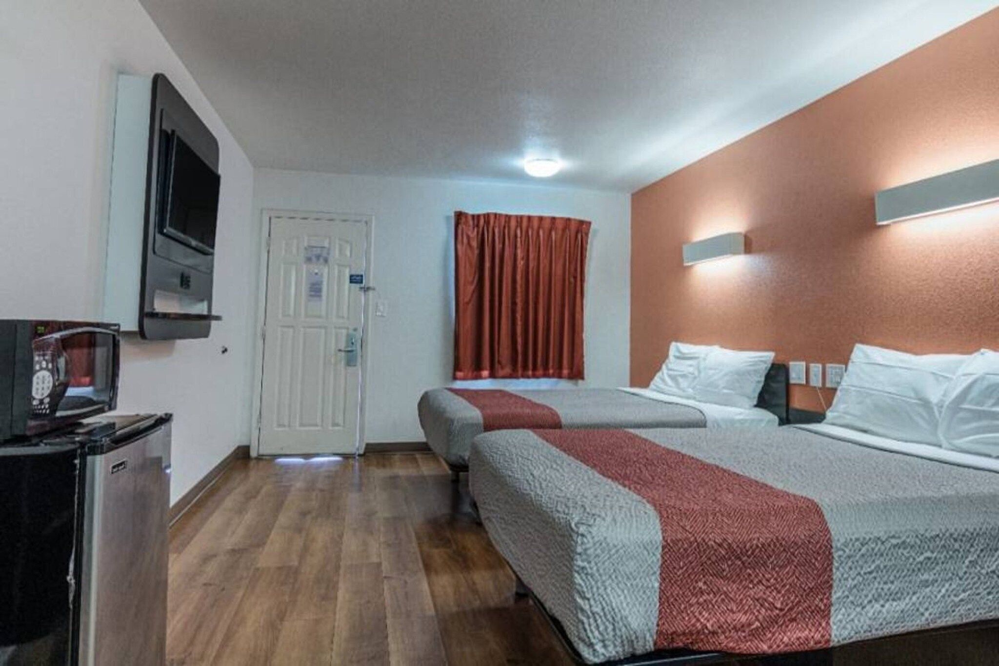 Une chambre d’hôtel avec deux lits, une télévision, une porte et une fenêtre avec des rideaux.