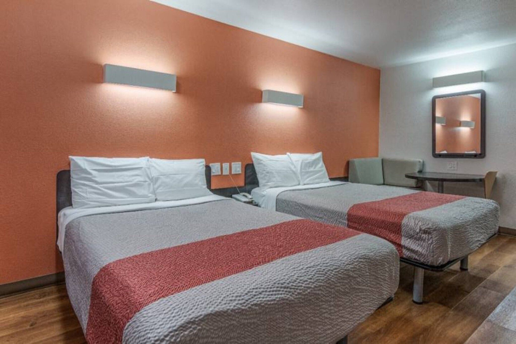Quarto de hotel com duas camas, uma mesa pequena e uma cadeira.