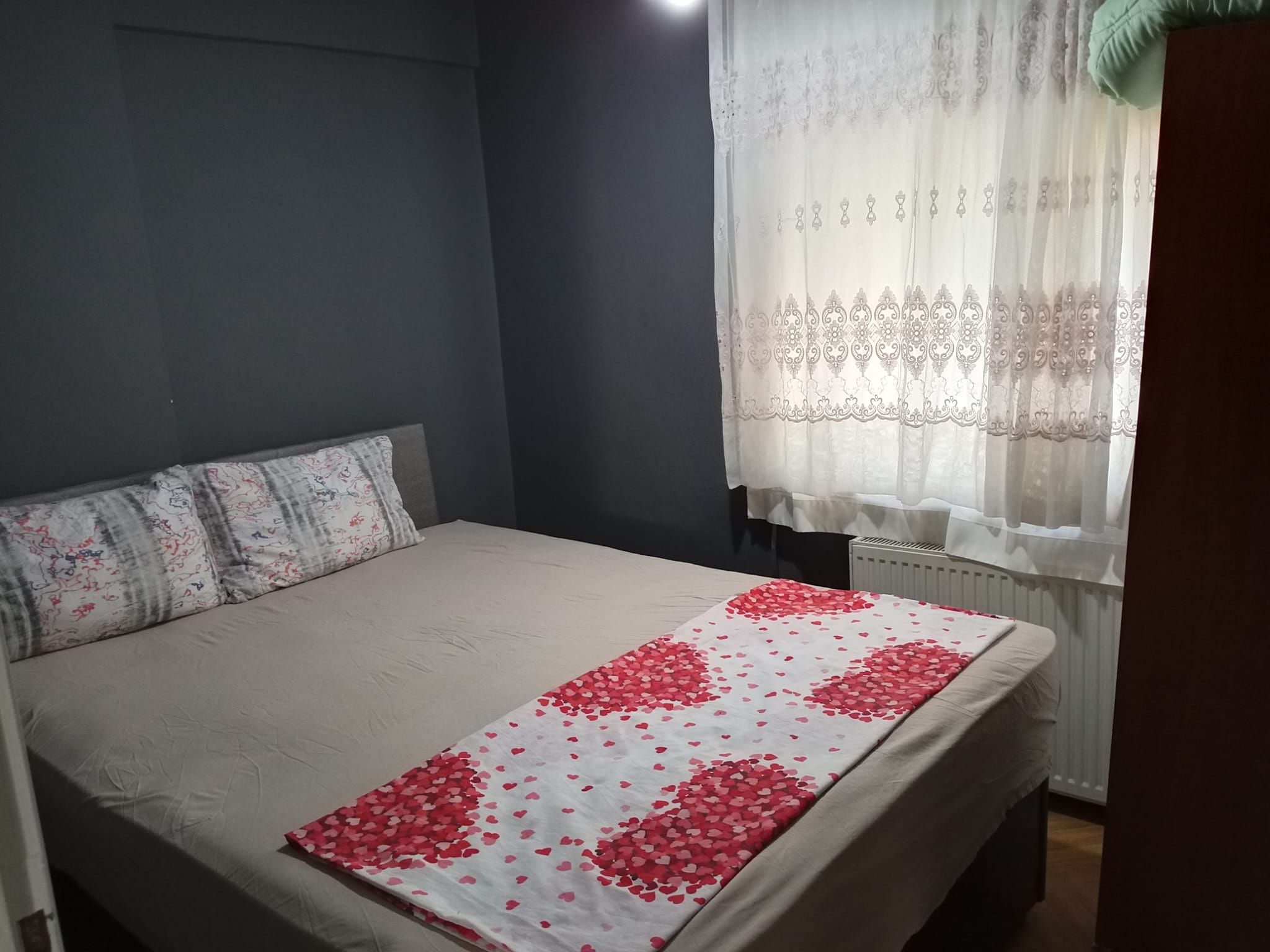Un dormitorio con una cama, un ventanal con cortinas traslúcidas y un radiador.