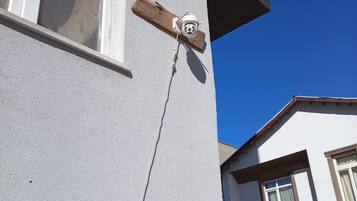A building corner with a white exterior, a window, and a security camera mounted on a wooden beam.