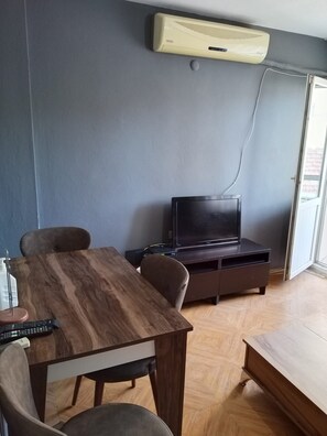 Ein modernes Wohnzimmer mit Esstisch aus Holz, einer Couch, einem Flachbildfernseher und einer eingebauten Klimaanlage.