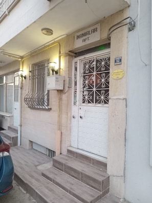 A building entrance with a white door, metal window grills, and a sign above the door.