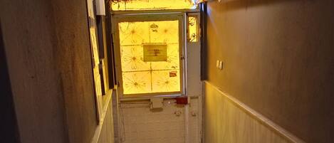 Un couloir avec un plancher en bois, une porte avec une pancarte et un luminaire au plafond.