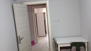 Ein Schlafzimmer mit einem Bett, einem Schreibtisch und einem Stuhl. Eine Tür führt in einen anderen Raum.