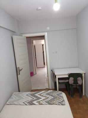 Ein Schlafzimmer mit einem Bett, einem Schreibtisch und einem Stuhl. Eine Tür führt in einen anderen Raum.
