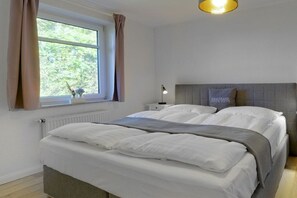 Ein Schlafzimmer mit einem Bett, einem Nachttisch, einer Lampe, einem Fenster mit Vorhängen und einer Heizung.
