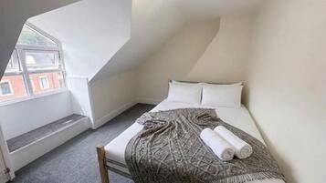 A bedroom with a sloped ceiling, a bed with a patterned blanket, and a window overlooking a building.