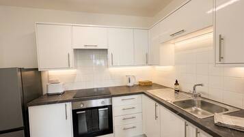 A modern kitchen with white cabinets, a black countertop, a built-in oven, a sink, and a kettle.