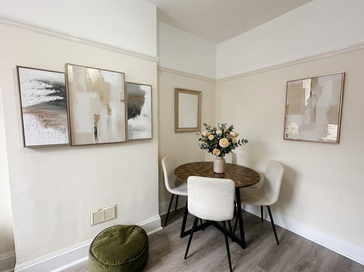 A dining area with a round table, four chairs, and three wall-mounted abstract paintings.