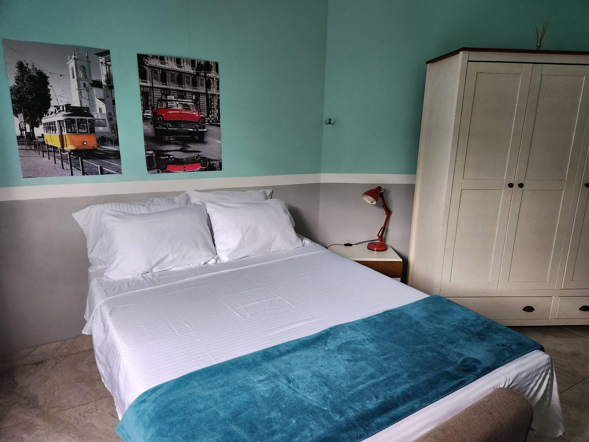 A bedroom with a bed, a nightstand, a lamp, a wardrobe, and two wall-mounted pictures.