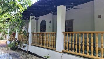 A covered outdoor area with a tiled floor, a wooden railing, and a ceiling fan.