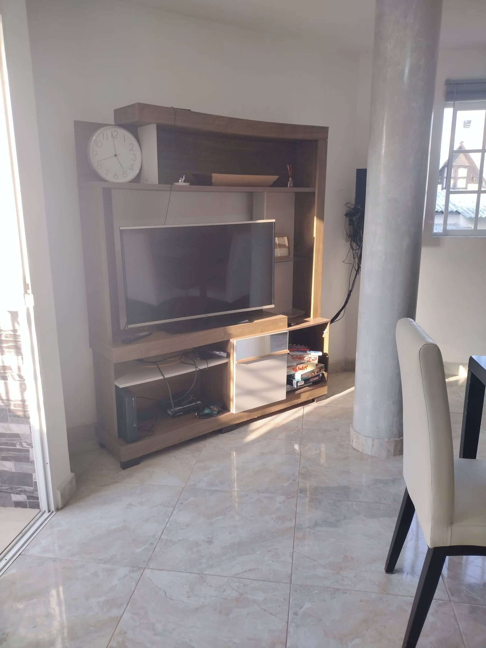 A living room with a flat-screen TV, wooden entertainment unit, and a chair.