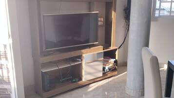 A living room with a flat-screen TV, wooden entertainment unit, and a chair.
