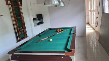 A pool table with balls and cues, a billiard rack, and overhead lighting.