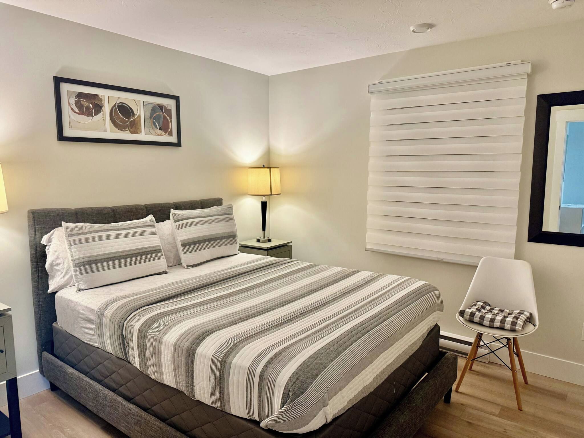 A neatly arranged bedroom with a bed, bedside lamps, a chair, and a window with blinds.
