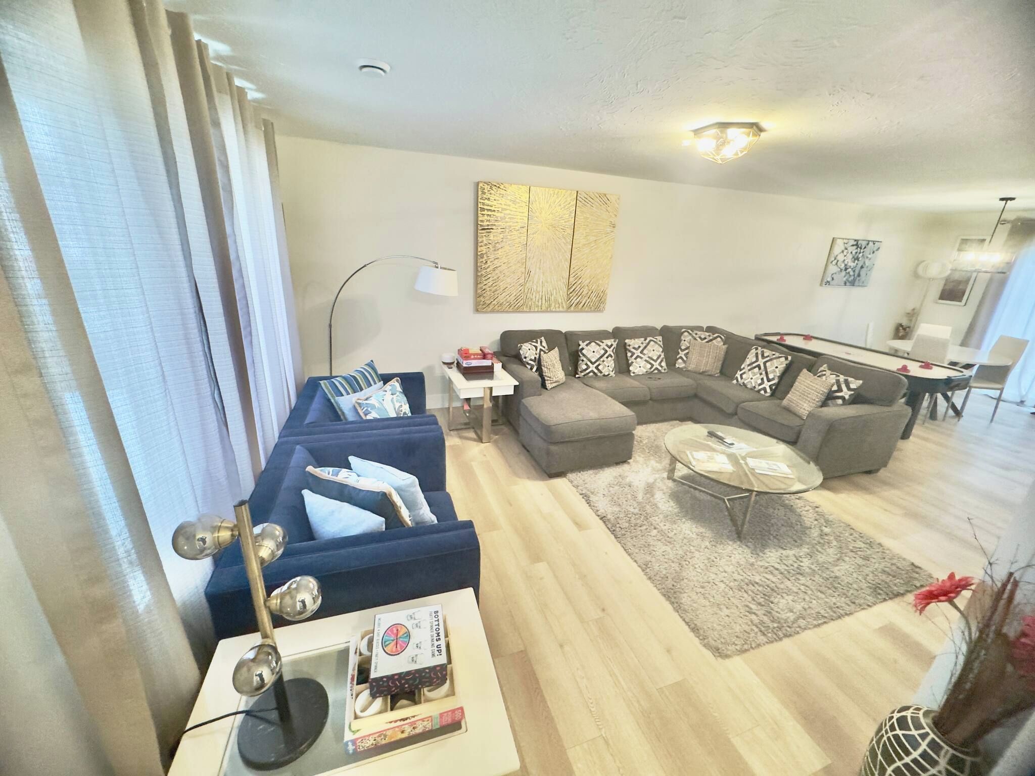 A modern living room with a sectional sofa, a glass coffee table, and a dining area with a white table and chairs.