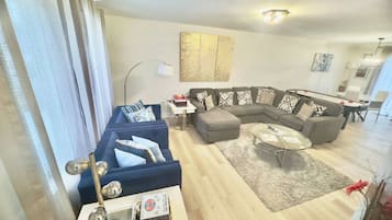 A modern living room with a sectional sofa, a glass coffee table, and a dining area with a white table and chairs.