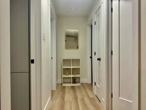 Un pasillo con puertas blancas, un espejo en la pared y una estantería con adornos.