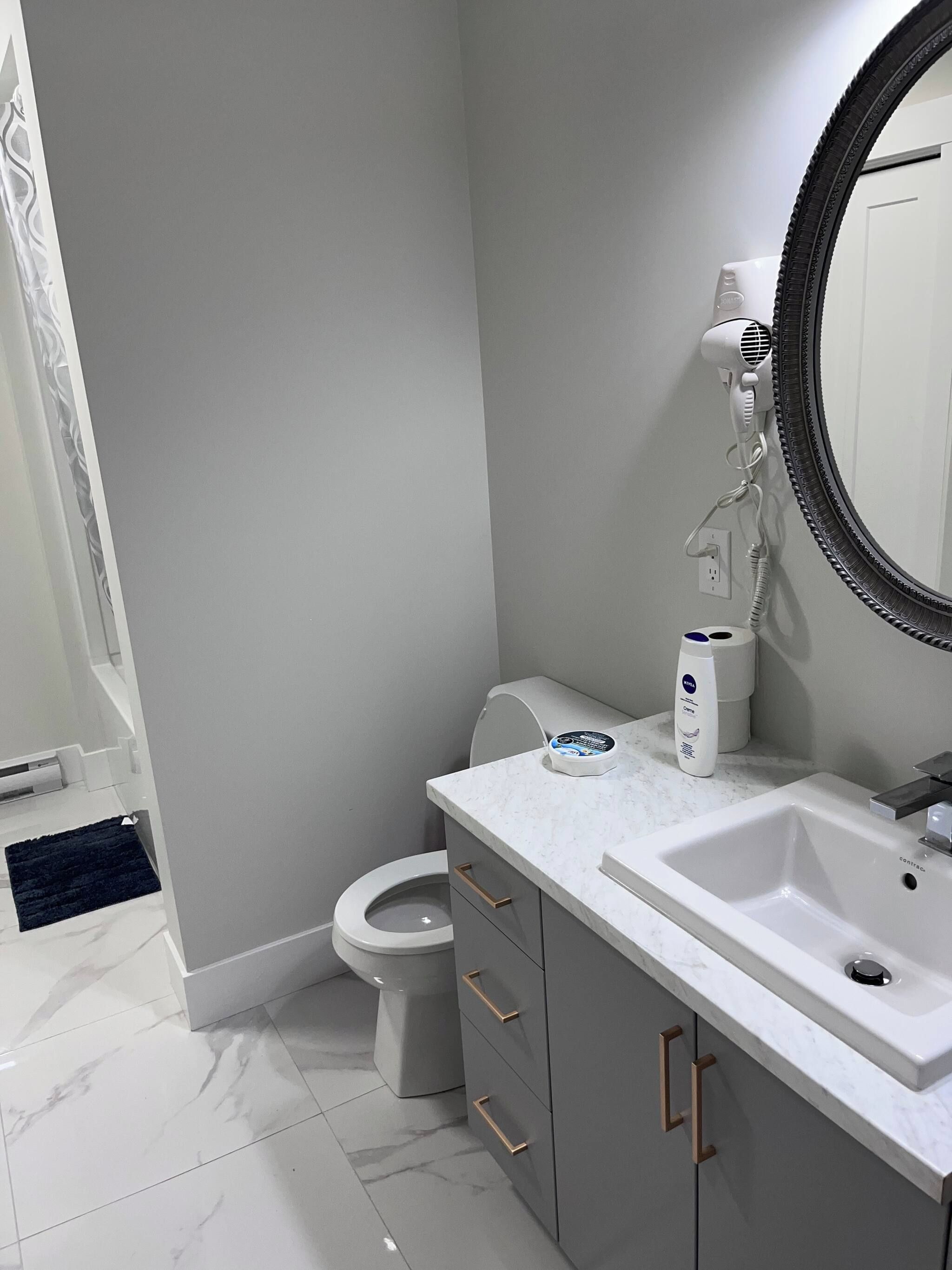 A modern bathroom with a white toilet, a sink with a mirror, and a hairdryer mounted on the wall.