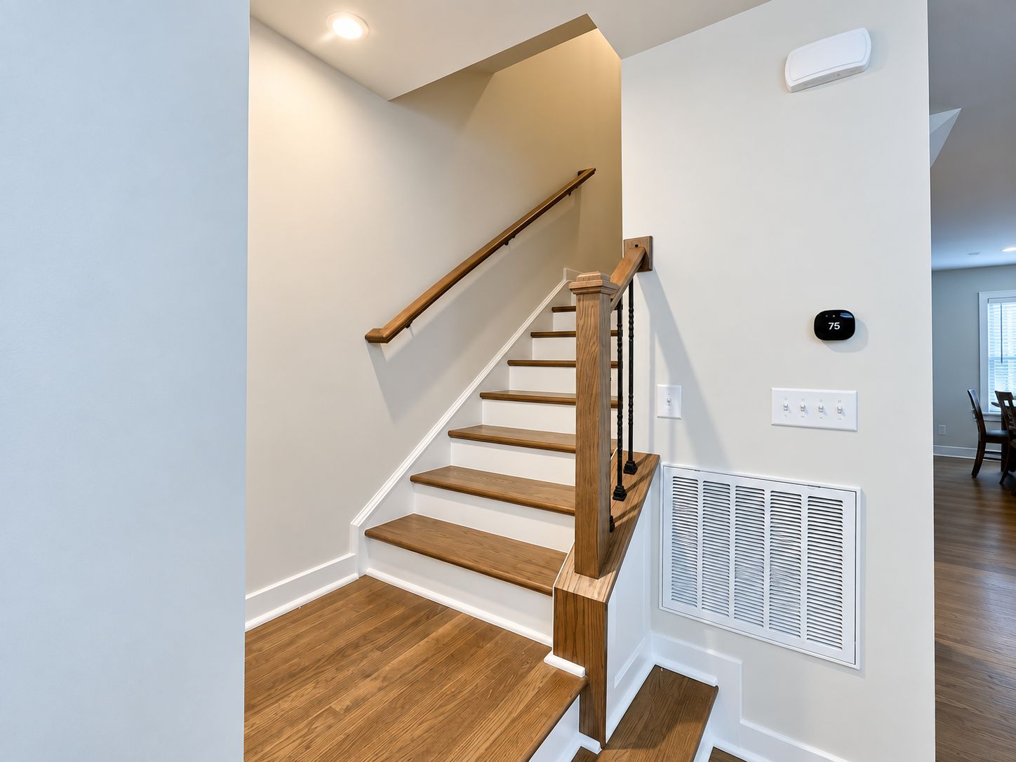 A staircase with wooden steps and a handrail, a wall-mounted thermostat, and a vent on the adjacent wall.