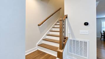 A staircase with wooden steps and a handrail, a wall-mounted thermostat, and a vent on the adjacent wall.