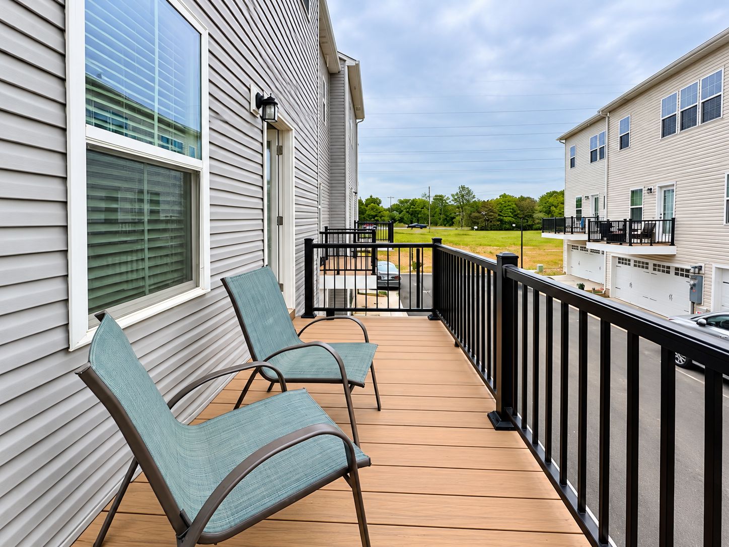 A wooden deck with two chairs, a railing, and a view of a residential area.