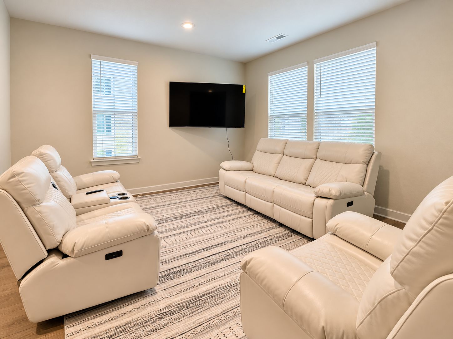 A living room with a flat-screen TV mounted on the wall, two beige sofas, and a patterned rug.