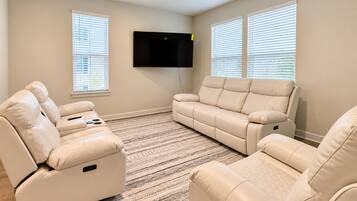 A living room with a flat-screen TV mounted on the wall, two beige sofas, and a patterned rug.