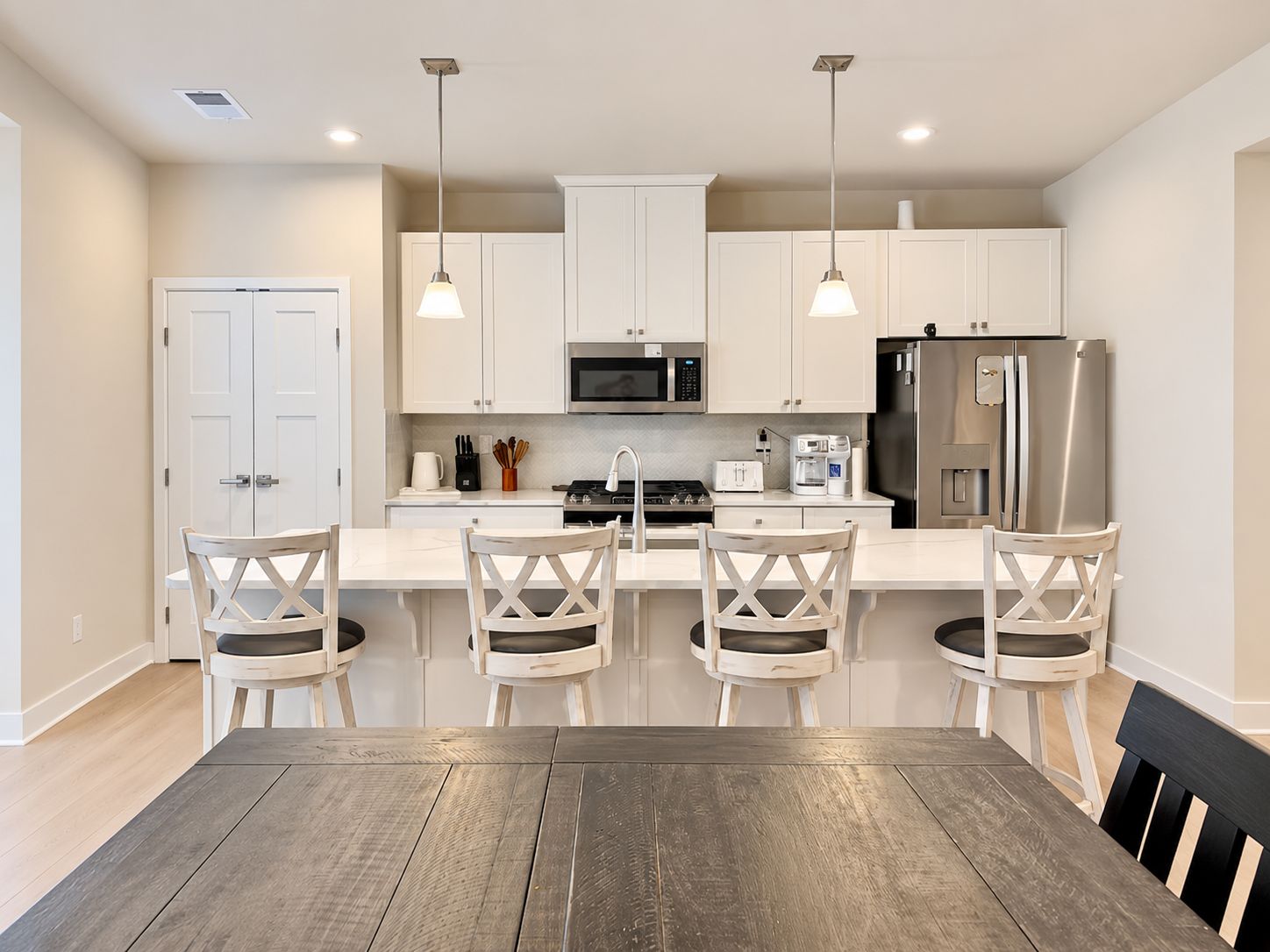 Eine moderne Küche mit weißen Schränken, Edelstahlgeräten und einem Holzespeisetisch mit vier Stühlen.