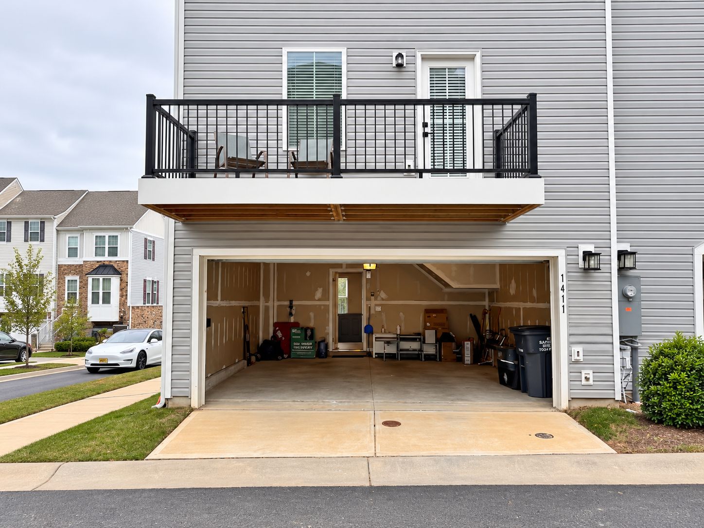A two-story residential building with a covered garage entrance, a balcony with a black railing, and a visible mailbox.