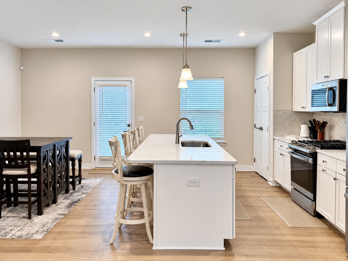 Een moderne keuken met een centraal eiland, witte kasten en een eethoek met houten stoelen.