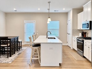 Een moderne keuken met een centraal eiland, witte kasten en een eethoek met houten stoelen.