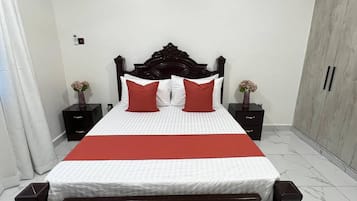 Une chambre à coucher comprenant un lit, des tables de chevet, une armoire et un ventilateur de plafond.