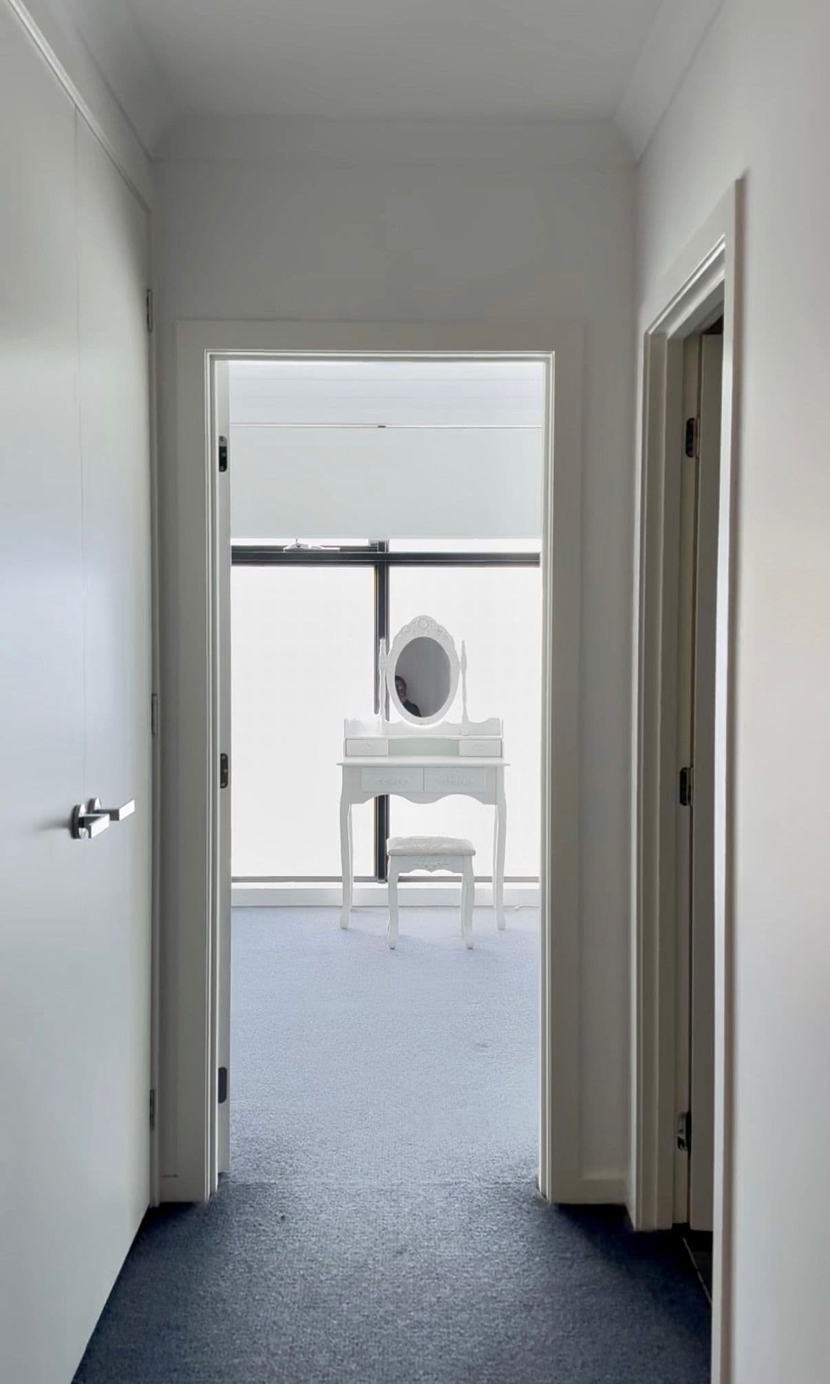 A hallway leading to a room with a white vanity and a large mirror.